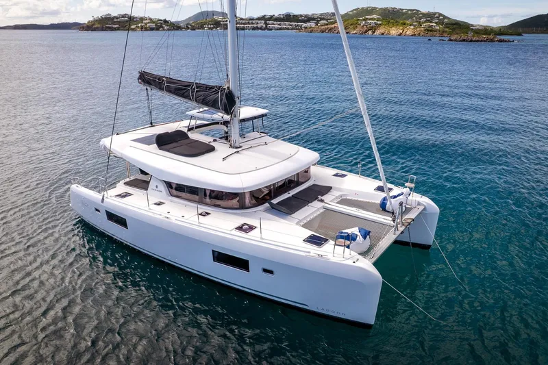 Good Times And Tan Lines Yacht Photos Pics 2023 Lagoon 42 catamaran sailing in clear blue waters near scenic coastline.