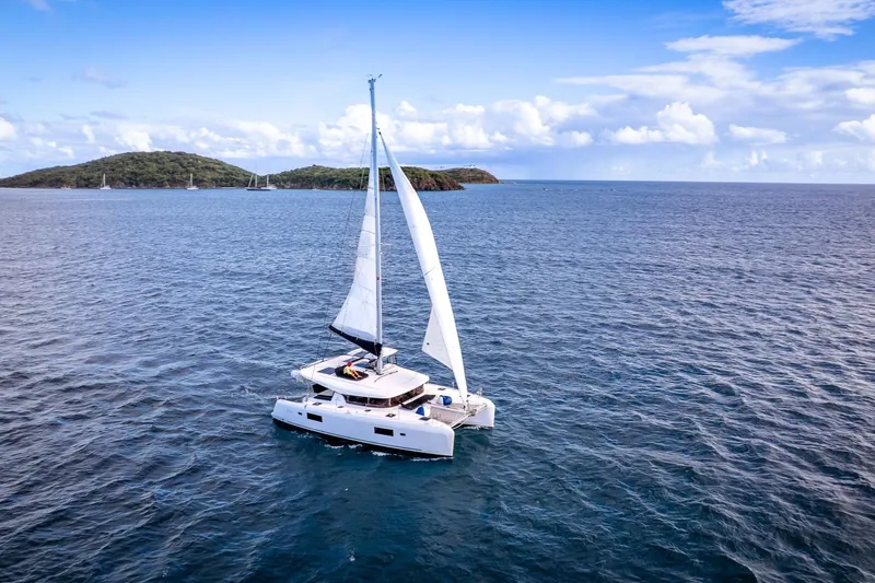 Good Times And Tan Lines Yacht Photos Pics 2023 Lagoon 42 catamaran sailing on open sea with islands in background.