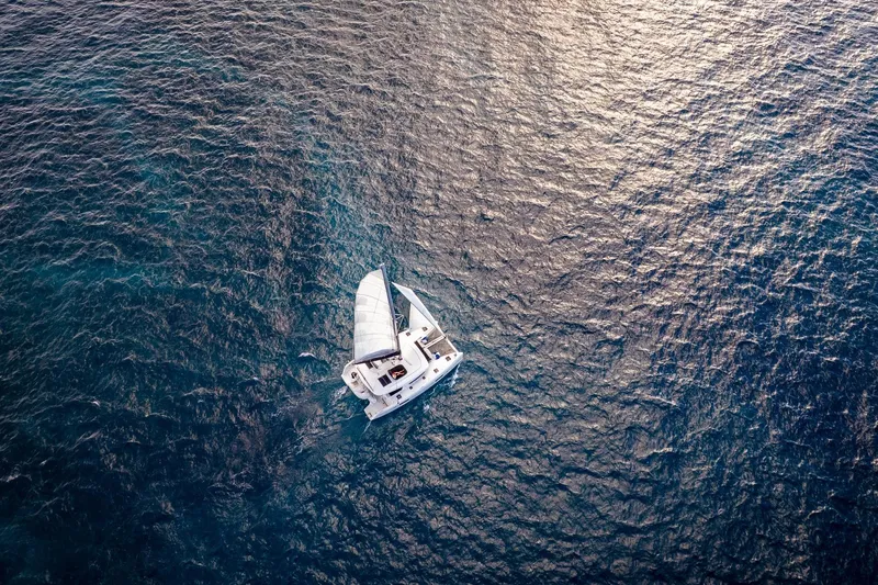 Good Times And Tan Lines Yacht Photos Pics Aerial view of 2023 Lagoon 42 catamaran sailing on open ocean waters.