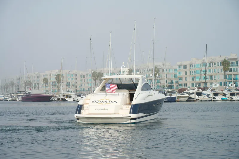 Distraction Yacht Photos Pics Sunseeker Camargue 50 yacht, 2000 model, cruising in a marina with modern buildings.