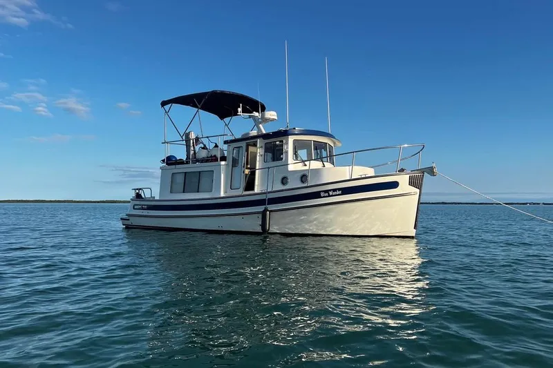 Blue Wander Yacht Photos Pics 2023 Nordic Tug 34 Tug boat anchored on calm water under clear blue sky.