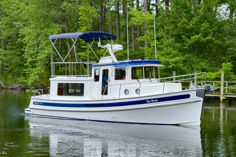 Blue Wander Yacht Photos Pics 2023 Nordic Tug 34 cruising on a serene, tree-lined waterway.