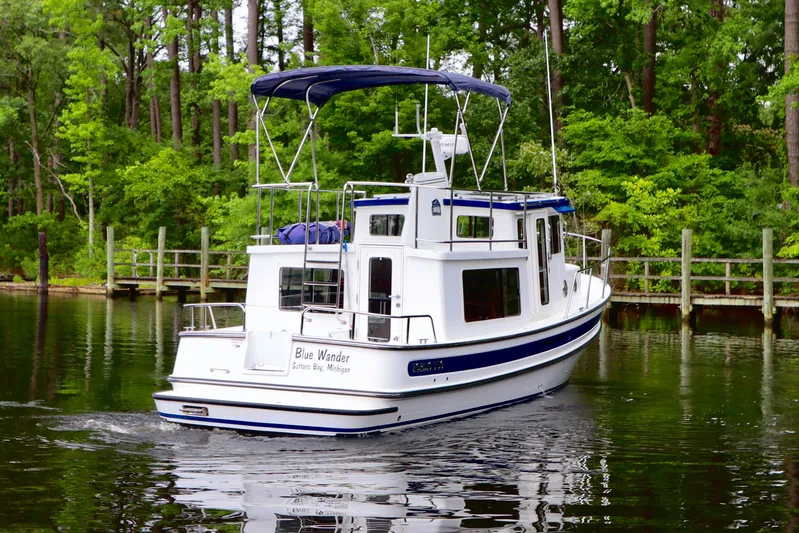 Blue Wander Yacht Photos Pics 2023 Nordic Tug 34 cruising on a serene, tree-lined waterway.