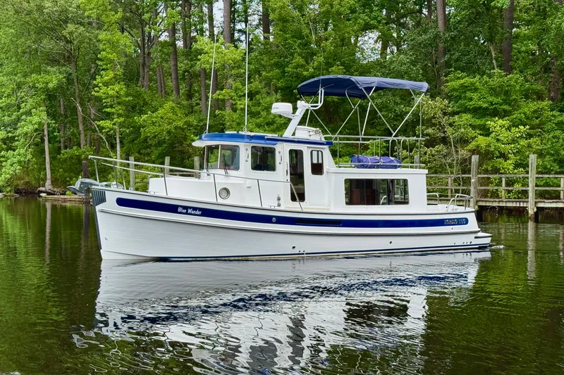 Blue Wander Yacht Photos Pics 2023 Nordic Tug 34 cruising on a serene, tree-lined waterway.