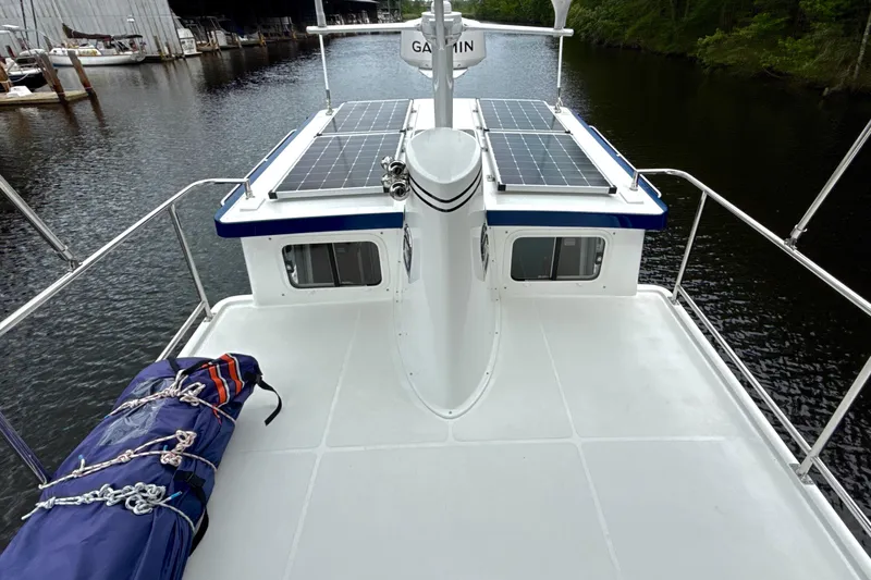 Blue Wander Yacht Photos Pics 2023 Nordic Tug 34 Tug with solar panels on deck, docked by a river.