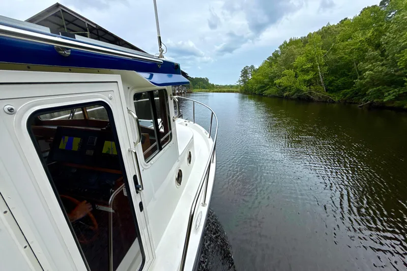 Blue Wander Yacht Photos Pics 2023 Nordic Tug 34 navigating a serene river with lush green surroundings.
