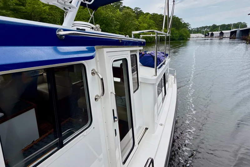 Blue Wander Yacht Photos Pics 2023 Nordic Tug 34 cruising on a serene waterway, surrounded by lush greenery.