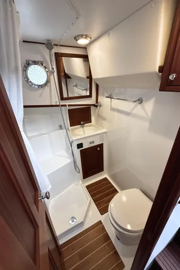 Blue Wander Yacht Photos Pics 2023 Nordic Tug 34 Tug bathroom with shower, sink, and toilet, featuring wood accents and porthole.