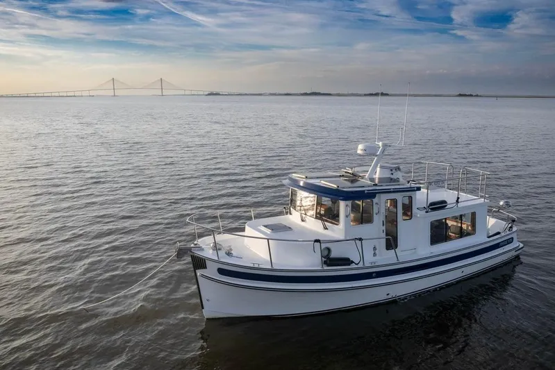 Blue Wander Yacht Photos Pics 2023 Nordic Tug 34 Tug on calm water with bridge in background.