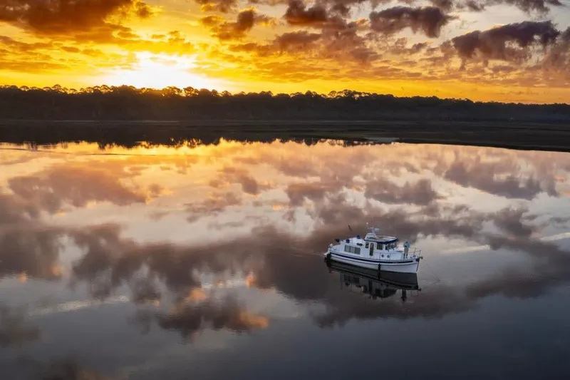 Blue Wander Yacht Photos Pics 2023 Nordic Tug 34 on tranquil water at sunset, reflecting vibrant sky.