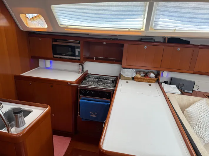 Passion Place Yacht Photos Pics Interior of 2007 Beneteau 49 yacht kitchen with stove, microwave, and wooden cabinetry.