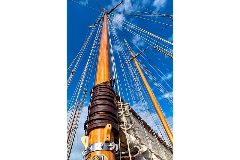 Invader Yacht Photos Pics Tall mast of 1905 Gaff Schooner by G. LAWLEY & Son, against blue sky.