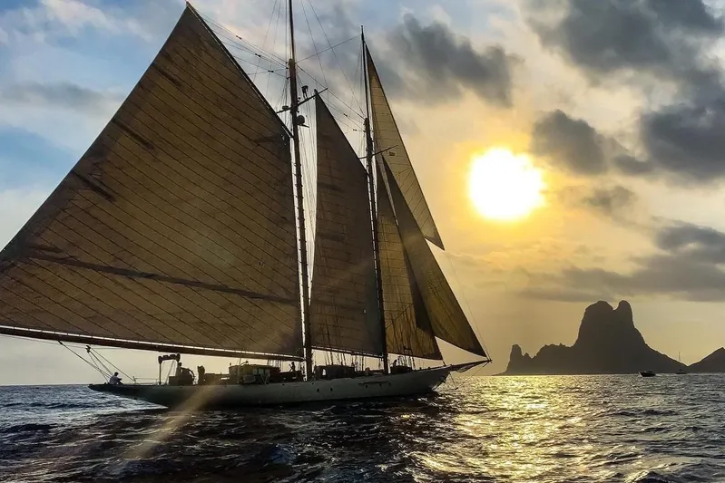Invader Yacht Photos Pics Vintage 1905 Gaff Schooner sailing at sunset near rocky coastline.