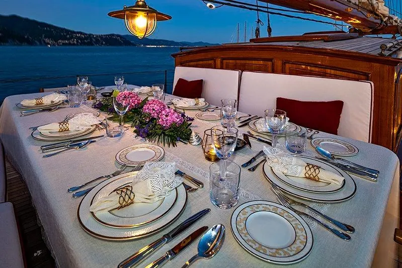 Invader Yacht Photos Pics Elegant dining setup on 1905 Gaff Schooner by G. LAWLEY & Son, overlooking serene waters.