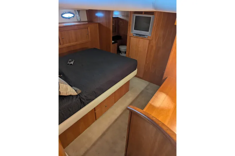 Impulse Yacht Photos Pics 2004 Navigator 57 yacht bedroom with wood paneling, bed, TV, and porthole window.
