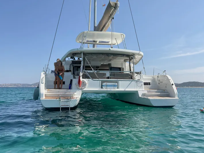 Martina Yacht Photos Pics 2021 Lagoon 46 catamaran anchored in clear blue water, with a person sitting on the deck.