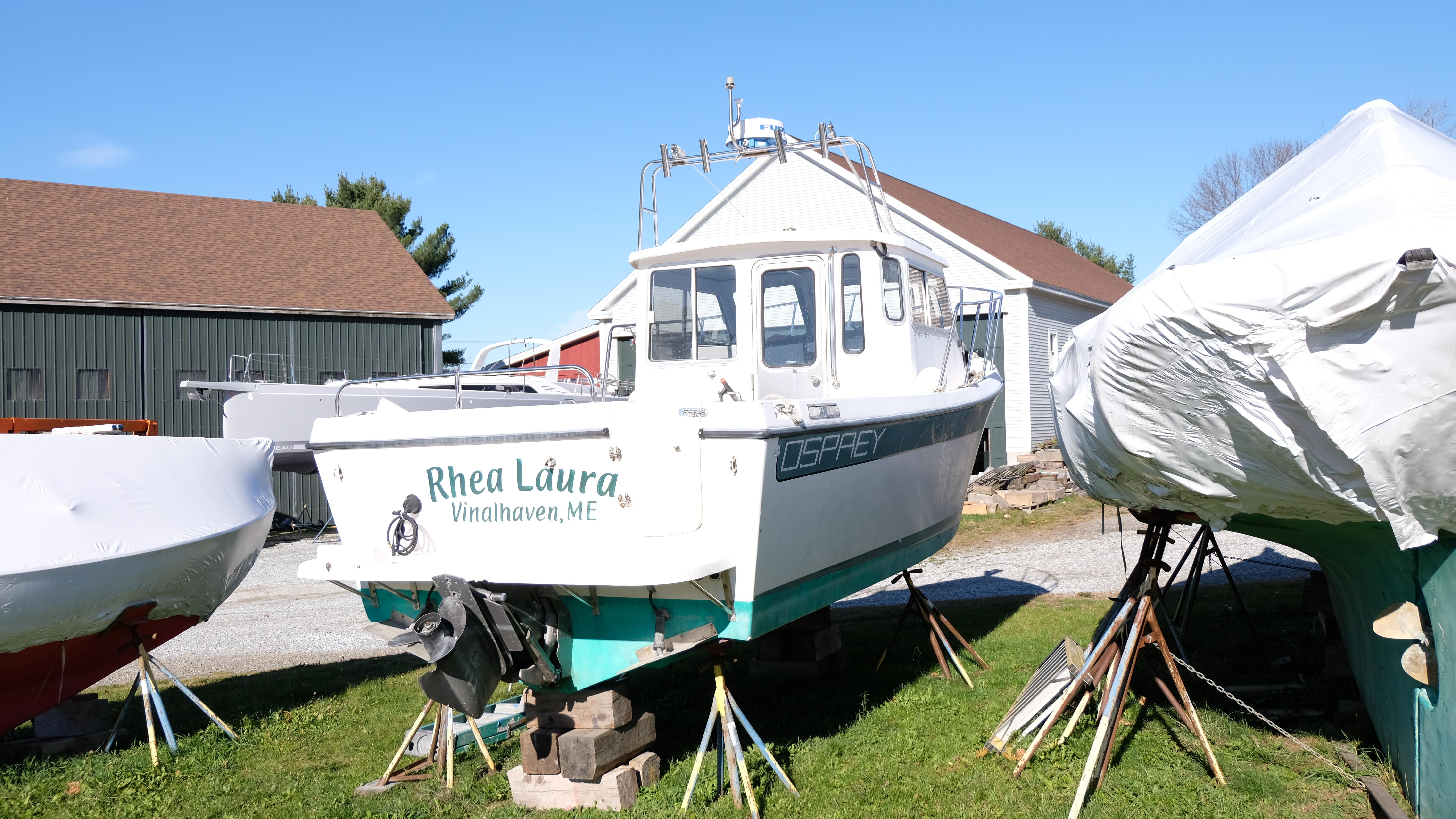 1999 Osprey 24 boat named "Rhea Laura" on stands in a yard.