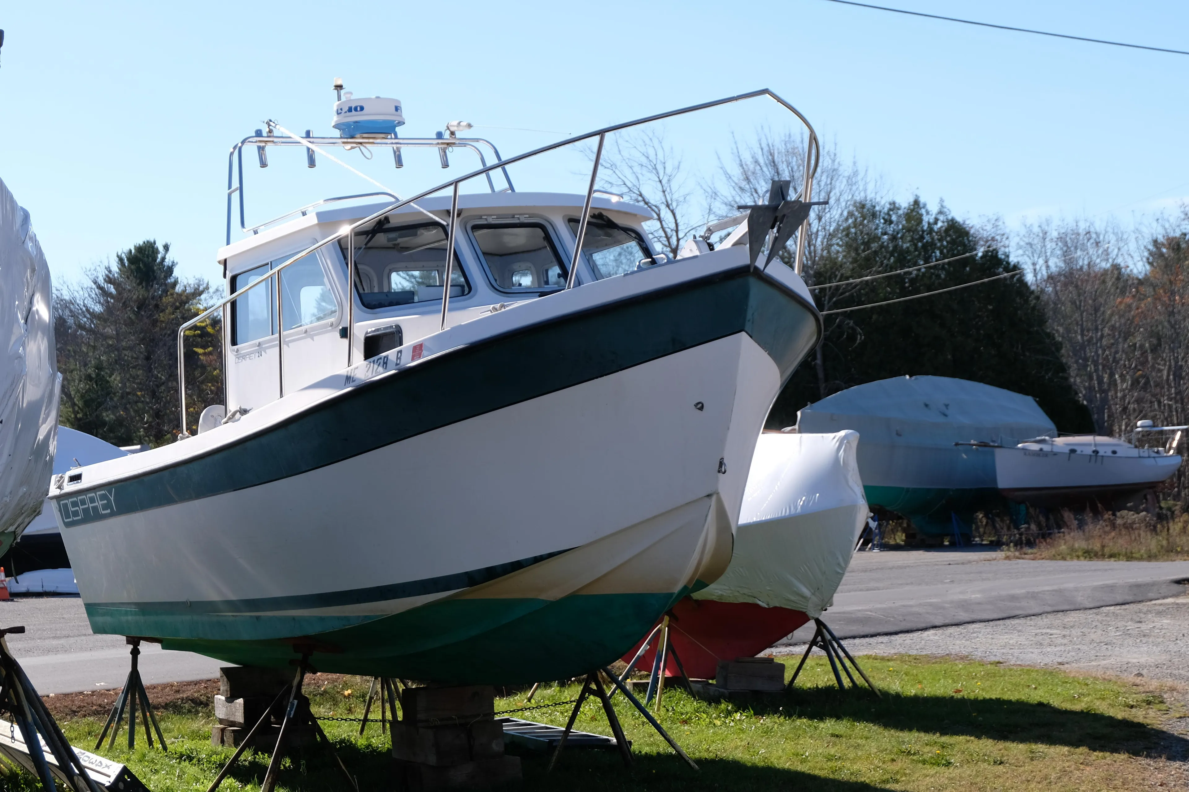 1999 Osprey 24 boat on stands, outdoor storage, clear day, trees in background.