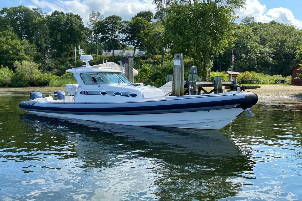 2011 Protector Tauranga 41 boat docked on calm water, surrounded by lush greenery.