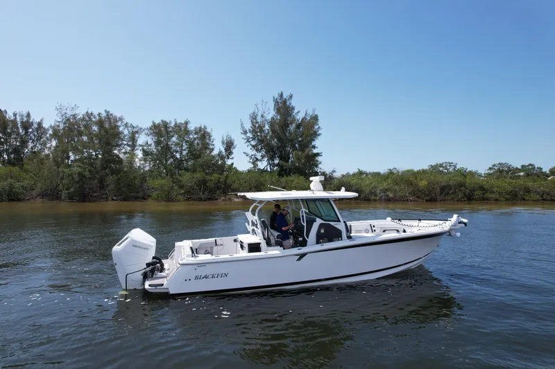  Yacht Photos Pics 2024 Blackfin 332 CC boat cruising on calm water near a forested shoreline.