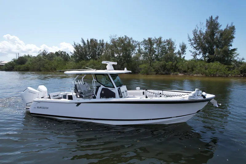  Yacht Photos Pics 2024 Blackfin 332 CC boat on calm water, surrounded by lush greenery.