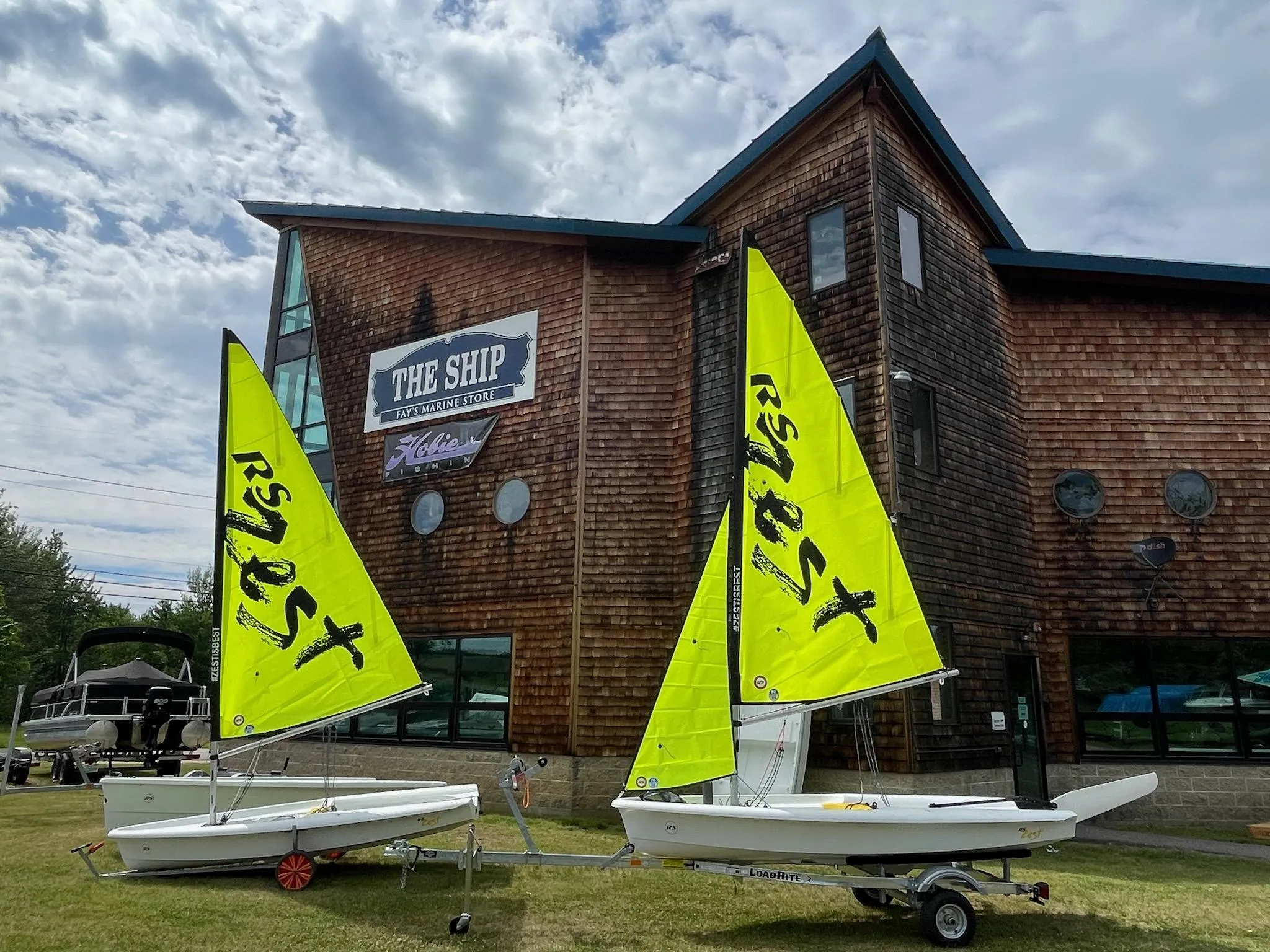 Two RS Zest sailboats with bright yellow sails in front of a rustic building.