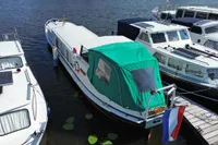 Custom 1958 boat with green canopy docked beside other vessels on a sunny day.