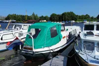 A 1958 custom boat with a green canopy docked at a marina, surrounded by other boats.