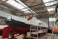 Custom 1958 boat under restoration in a workshop with scaffolding and high ceilings.