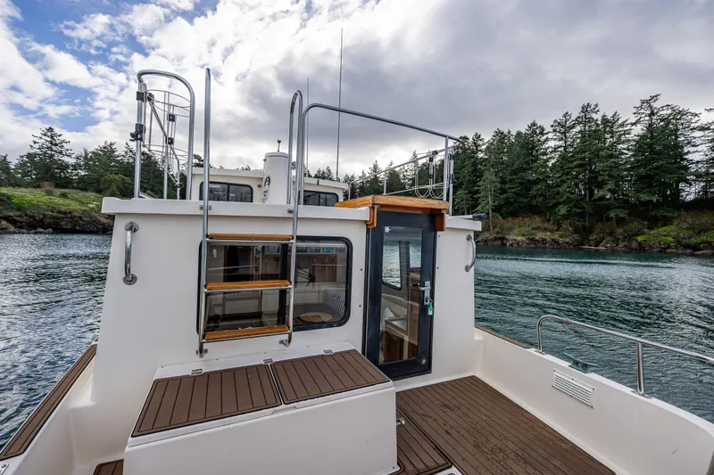 Artemis Yacht Photos Pics 1999 Nordic Tug 32 on serene water, surrounded by lush greenery and cloudy sky.