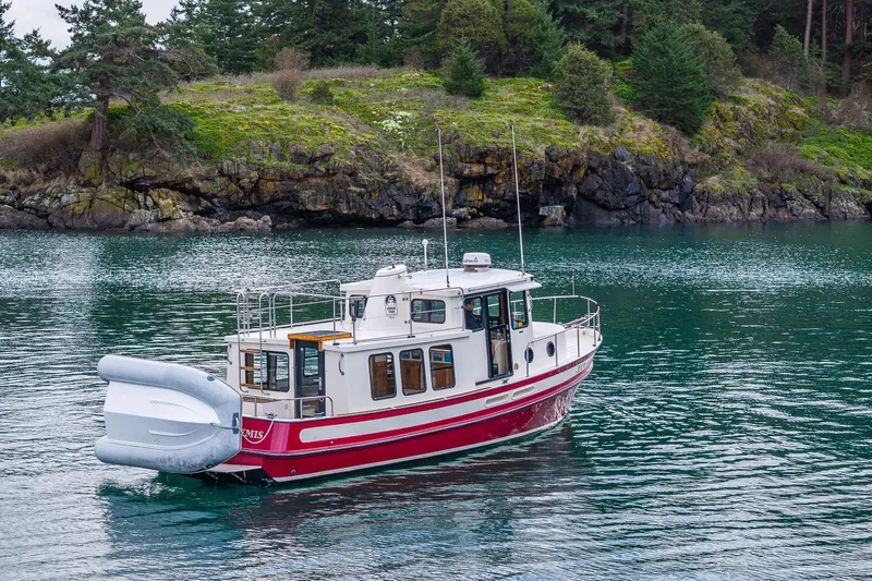 Artemis Yacht Photos Pics 1999 Nordic Tug 32 boat on calm water near a rocky, forested shoreline.