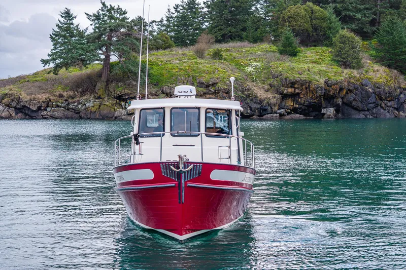 Artemis Yacht Photos Pics Red 1999 Nordic Tug 32 boat on calm water near rocky shoreline.