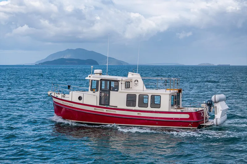 Artemis Yacht Photos Pics Red 1999 Nordic Tug 32 cruising on the ocean with distant islands in the background.