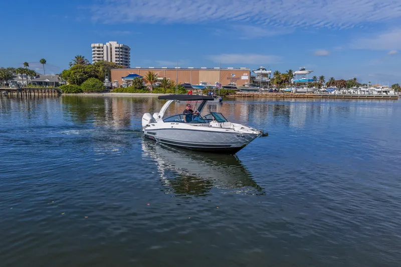  Yacht Photos Pics 2023 Monterey 305SS Super Sport boat cruising on a calm waterfront with buildings in the background.
