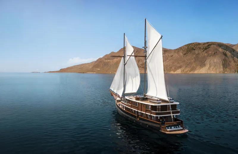 Jiva Ananta Yacht Photos Pics Sailing yacht Phinisi Custom 2027 on calm sea with mountainous backdrop.