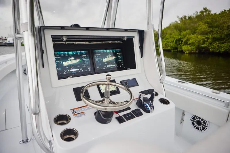  Yacht Photos Pics 2026 Contender 32 ST boat dashboard with dual screens and steering wheel, near lush shoreline.