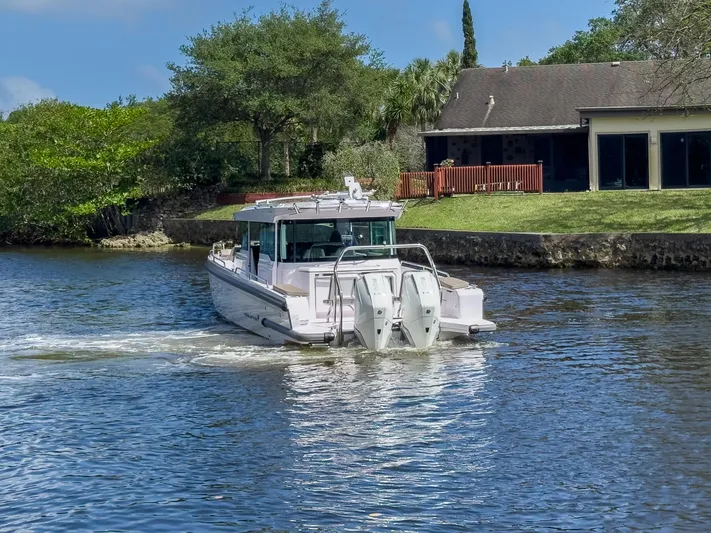  Yacht Photos Pics 2024 Axopar 37XC CROSS CABIN boat cruising on a serene river near a house.