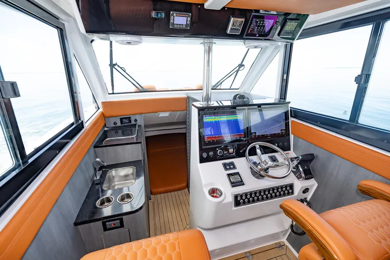  Yacht Photos Pics 2023 Invincible 46 Pilothouse interior with modern helm, orange seating, and navigation equipment.