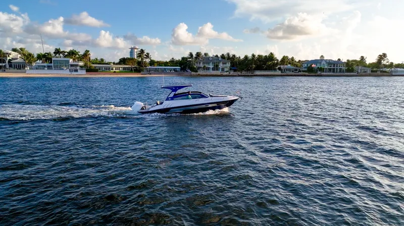  Yacht Photos Pics 2024 Hanover 305 boat cruising on a sunny day near a coastal residential area.
