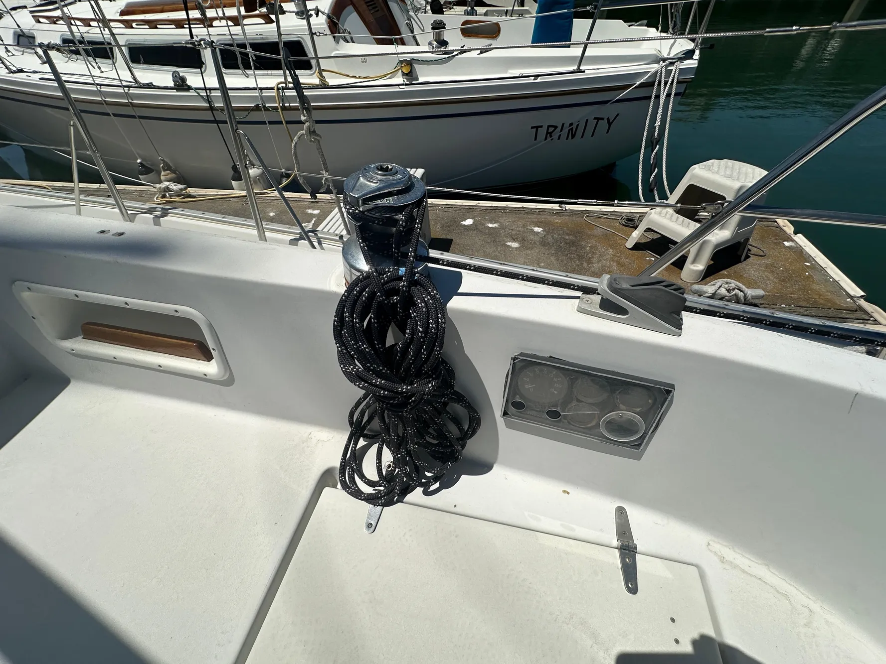 Sailboat deck with coiled rope, Nonsuch Ultra 1986, docked near another boat named Trinity.