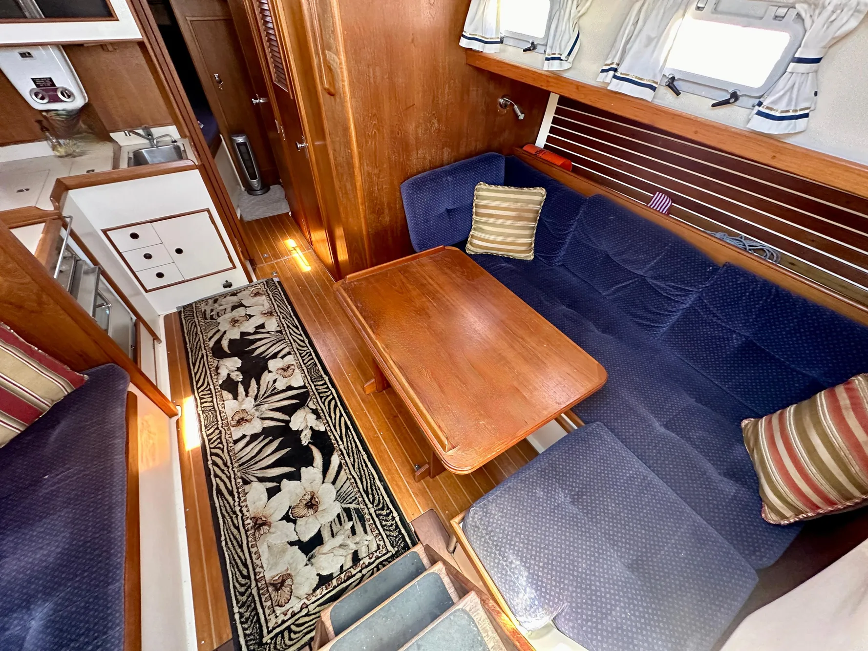 Cozy 1986 Nonsuch Ultra yacht interior with blue seating, wooden table, and floral rug.