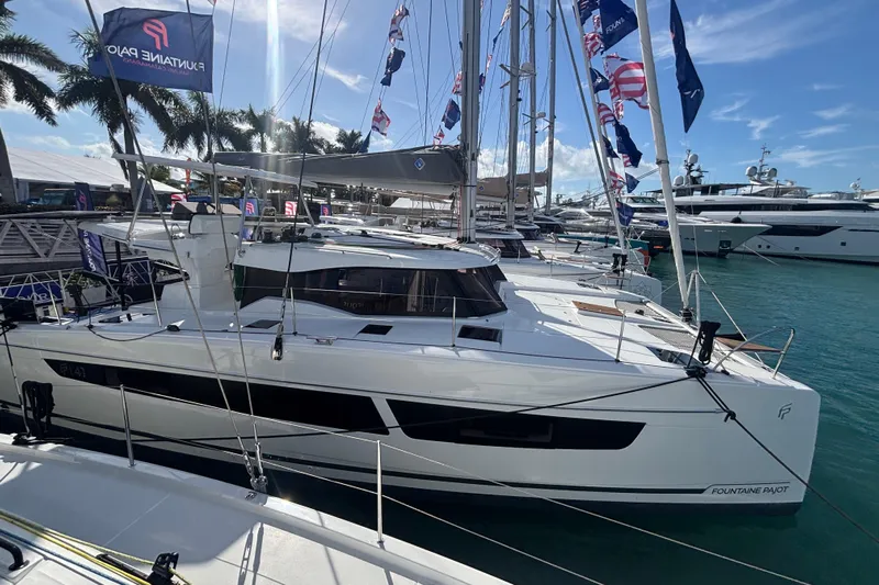 The Ilusion Yacht Photos Pics 2025 Fountaine Pajot 41 catamaran docked at marina, surrounded by yachts and palm trees.