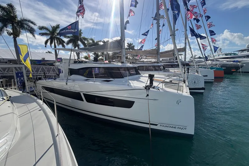 The Ilusion Yacht Photos Pics 2025 Fountaine Pajot 41 catamaran docked at marina, surrounded by flags and palm trees.