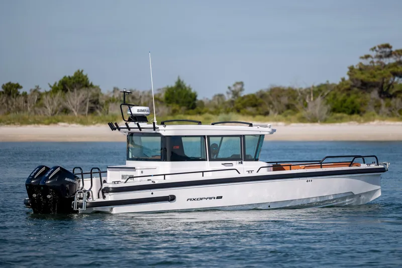 Yacht Photos Pics 2024 Axopar 28 CABIN boat cruising on calm water near a sandy shoreline.