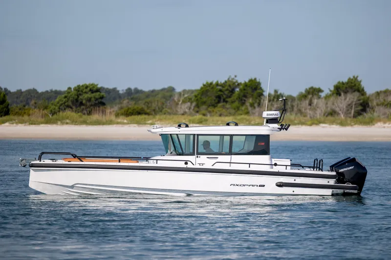  Yacht Photos Pics 2024 Axopar 28 CABIN boat cruising on calm water near a scenic shoreline.