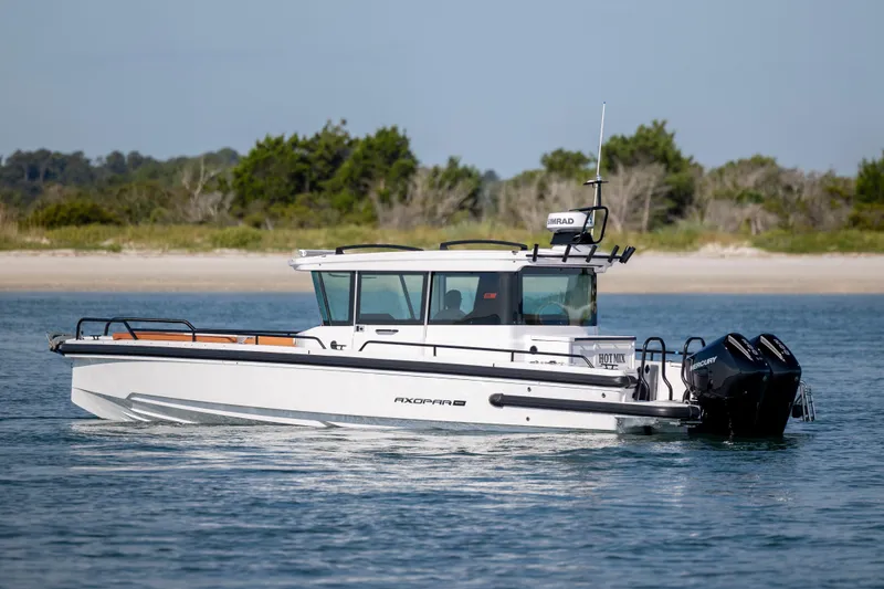  Yacht Photos Pics 2024 Axopar 28 CABIN boat cruising on calm water near a sandy shoreline.