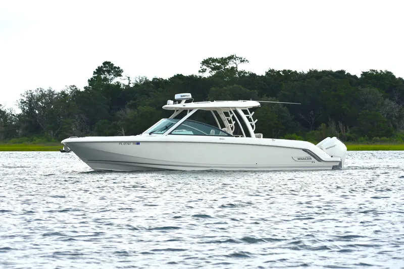  Yacht Photos Pics 2023 Boston Whaler 320 Vantage boat cruising on a calm lake with forested background.