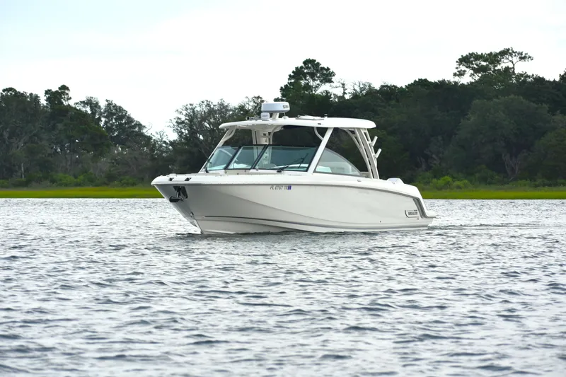  Yacht Photos Pics 2023 Boston Whaler 320 Vantage cruising on a serene lake with lush greenery.