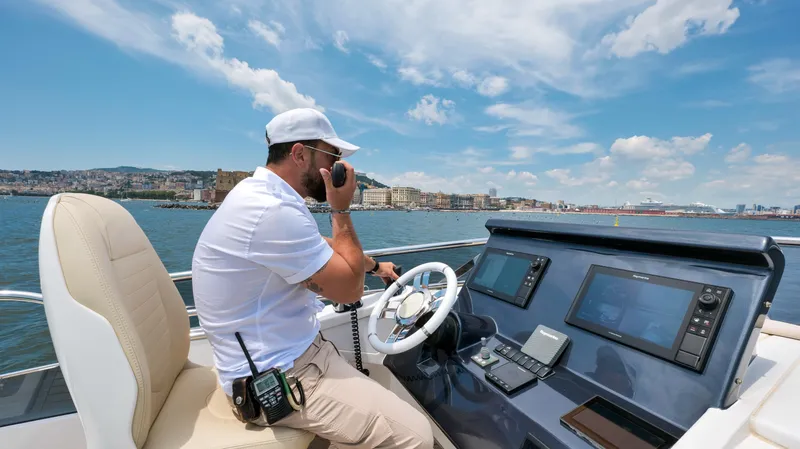 Elisa II Yacht Photos Pics Man operating 2018 Azimut 77 S yacht, using radio communication, with cityscape in background.