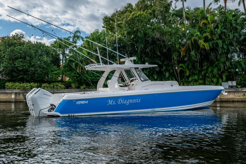 Mrs Diagnosis Yacht Photos Pics 2020 Intrepid 407 Panacea boat, blue hull, docked on calm water, lush greenery background.